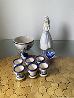 Group photo showing the ceramic egg cups, ceramic bowl, art glass bird, paperweight, and ceramic lady figurine on a gold placemat