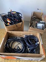 Three boxes filled with assorted audio/visual and power cables including RCA wires and speaker wires.