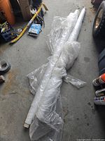 Photo of two large rolls of clear plastic dropsheet flooring covering, lying on a concrete floor.