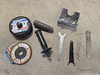 Full view of grinder cut off wheels, handles, wheel guard, and 4 metal wrenches/spanners.
