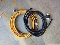 Two heavy duty RV extension cables, one yellow and one black, coiled on concrete floor with male and female plugs visible.