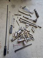 Assorted vintage Snap-on and Blue-Point tools, including socket wrenches, ratchets, pry bars, screwdriver, and multiple sockets laid out on a concrete floor.