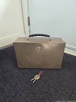 Closed metal cash box with black handle on top, keys placed in front for scale and verification.