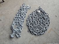 Full view of both metal chains side by side on concrete floor. One tightly coiled chain tagged, other folded loosely with hook.