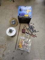 Overhead view of drill accessories including wire brush wheel, hole saw with mandrel, sanding drum, various drill and screwdriver bits, and drill brush set box.