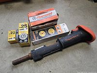 Ramset Hammershot powder-activated nailer with nails and powder cartridges on concrete floor.