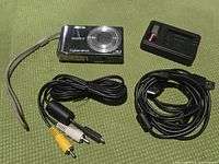 Sony Cybershot DSC-W370 camera with battery charger and cables laid out on green surface