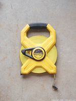 Top view of Stanley yellow measuring tape with black handle and crank, tape rolled inside plastic casing.