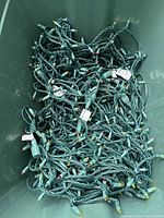Large plastic bin filled with multiple tangled strands of outdoor green-wire Christmas string lights with multi-colored bulbs.