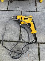 Yellow and black DeWalt electric drill with cord, resting on stone tile ground