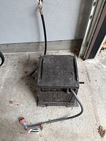Closed view of brown retractable hose reel box with attached hose and nozzle outside on concrete floor.