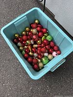 Large blue bin filled with over 50 assorted small to medium Christmas ornaments in red, gold, and green colors.