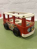Side view of the red and white Fisher Price Mini Bus showing decal wear and open roof with six figure seats inside.