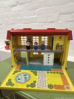 Front view of Fisher Price Children's Hospital playset opened showing two floors with Little People figures standing on the upper floor and painted outdoor scene on the lower door section