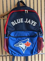 Full front view of navy blue kids backpack with Blue Jays text on top and bird logo on front pocket. Red mesh side pockets visible.