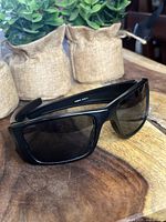 Oakley Fuel Cell sunglasses in black placed on a wooden surface with small burlap pots in the background.