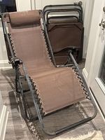Full view of one zero-gravity recliner chair showing brown mesh fabric attached to a rusted tubular metal frame.