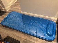 Photo of blue foam pineapple-shaped pool float laid flat on floor showing full length and embossed pineapple design with raised pillow section.