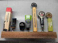 Image showing wooden base with six distinct beer tap handles, each with unique designs and branding.
