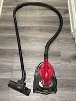 Full view of the vacuum cleaner showing body, hose, and floor vacuum attachment on floor.