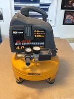 Front view of yellow and black Bostitch oil-free pancake air compressor with two gauges and integrated handle