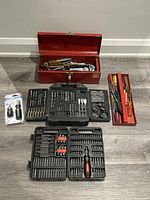 Full lot arranged showing red metal toolbox, two plastic drill bit cases, multi screwdrivers, and screwdriver set in tray.