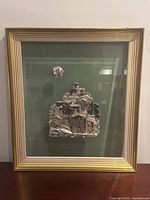 Full view of framed artwork showing the entire silver relief scene on green velvet background with gold and white frame.