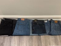 Eight pairs of men's jeans folded side-by-side in various colors and brands.
