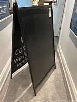 Black folding sandwich board shown from the front angle, displaying the blank black writable surface and metal frame.