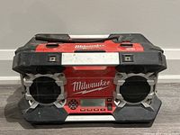 Front view of Milwaukee job site radio showing dual speakers with protective silver guards, Milwaukee logo and digital control panel beneath.