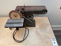 Front view showing the belt sander horizontally mounted with the disc sander on the left side and the base with power switch visible.