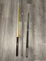 Full view of the two pool cues showing their length and design variation, placed on a grey wood floor.
