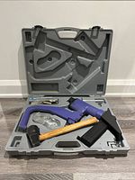 Blue Central Pneumatic pneumatic floor stapler, hammer, safety glasses, and staples in molded gray carrying case, displayed open against white wall.