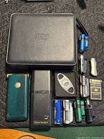Overview of entire lot showing portable humidor case, pocket humidors, cutter and assortment of lighters