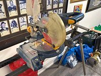 Full angled view of Ryobi miter saw showing red blade, blade guard, handle and dust collection bag hanging at rear.