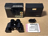 Overview of binoculars with original box, carrying case, strap, lens caps, and instruction manual arranged on flat surface