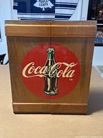 Full view of Coca-Cola wooden wall cabinet front with closed doors showing painted logo and wood grain.
