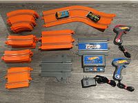 Top-down view of all track pieces, two slot cars, two handheld controllers, and power adapter laid out