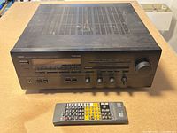 Front view of Yamaha RX-V870 stereo receiver with remote placed in front on table, showing control knobs, buttons, and display.