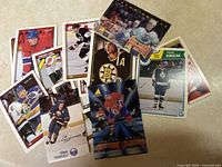 Photo of 14 assorted hockey cards spread out on a beige carpet floor showing different players and jerseys from various teams and eras.