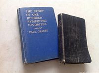 Photo of two pocket-sized books: 'The Story of One Hundred Symphonic Favorites' by Paul Grabbe with blue cover and gold text, and a smaller black book with a textured cover.