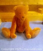 Full front sitting view of the golden brown plush teddy bear with movable arms and legs on a blue surface.