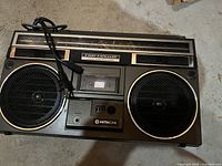 Front view of Hitachi boombox showing dual large 2-way speakers and cassette deck with power cord coiled on top