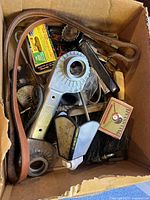 Top-down view of cardboard box filled with assorted various used items including belt, hardware, night light, matchbox, brush section.