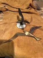 Pair of brass bird sculptures resting on a fabric backdrop showing their top views and stone bases.