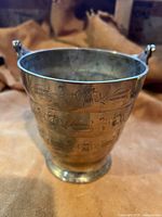 Front view of brass bucket showing floral engravings and handle attachment