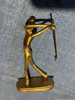 Side angle of brass golfer figurine showing the figure in mid swing with golf club raised behind.