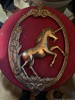 Front view of brass unicorn in an ornate oval frame with floral decoration, displayed on a red surface