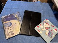 Photo showing two case covers and one spiral-bound address book displayed on a blue cloth.