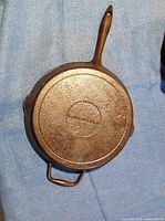 Full view of the cast iron frying pan showing the bottom side with two handles laying on a blue cloth.